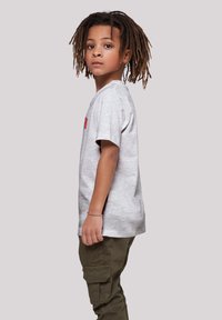 Camiseta de algodón gris con un corte relajado, construcción de costura lateral y mangas cortas, llevada con pantalones cargo verdes. Sin patrones ni detalles destacados.