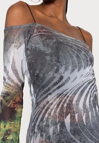 Haut à manches longues, décolleté épaule dénudée, en tissu transparent à motifs avec des tourbillons de gris, marron et vert. Fines bretelles.