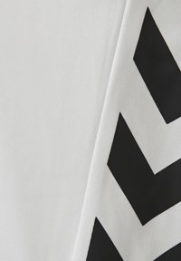 Witte stof met een gevouwen hoek die een patroon van drie zwarte naar beneden wijzende chevrons aan de rechterkant toont.