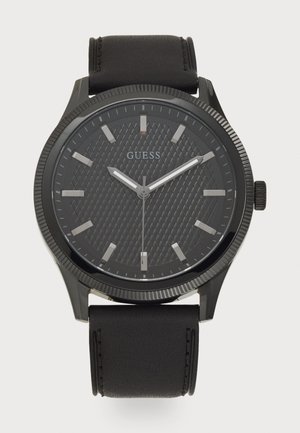 Montre analogique noire avec un cadran texturé noir, des index heures argentés et un bracelet en cuir noir. Présente une lunette striée et le logo de la marque.