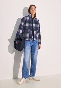 Gevlekt jasje in paars, groen en wit, met een kraag en zakken; gecombineerd met lichtblauwe flared jeans en witte sneakers.