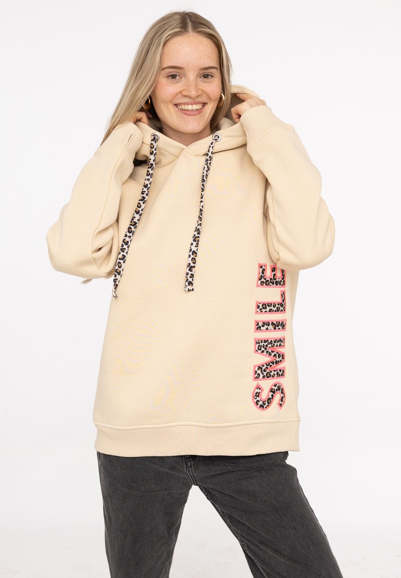 Sudadera color crema con un acento de estampado de leopardo en los cordones y la palabra "SONRÍE" en letras gruesas y con patrón en el lateral.