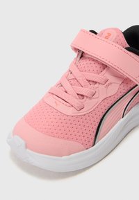 Chaussure de sport rose avec tige en mesh, lacets et bride Velcro, semelle blanche et accents noirs. Présente une surface texturée et un détail de logo.