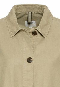 Beige jakke med krave, der har to brune knapper og et stribet accent indeni. Lavet af et let materiale.