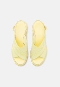 Sandali slingback gialli con cinturini incrociati che presentano il marchio "Calvin Klein", texture liscia e soletta imbottita per il comfort.