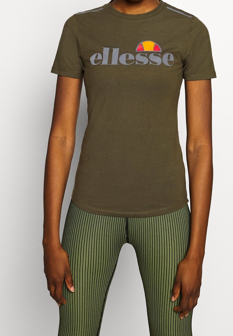 Olivově zelené upnuté tričko s kulatým výstřihem, na kterém je šedé logo "ellesse" a nad ním barevná grafika slunce.