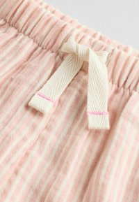 Tela a rayas rosas con una textura arrugada. Cintura elástica con un lazo crema y un detalle de costura en rosa.