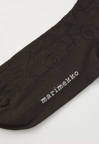 Barna zokni textúrált virágmintával és fehér "marimekko" logóval. Szövetből készült, sima felülettel és ívelt formával rendelkezik.