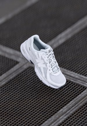 Hvid New Balance løbesko med mesh-overdel og snørebånd, der svæver over en metalristflade.