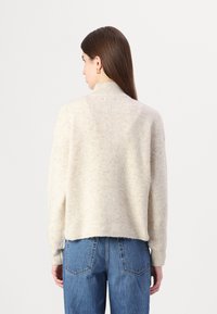 Strikket kremfarget genser med høy krage, ribbet tekstur og senkede skuldre, parret med høytaljede blå jeans.