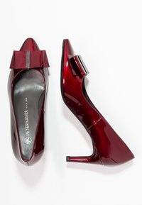 Escarpins en cuir verni rouge avec un bout pointu et un nœud décoratif à l'avant. Intérieur noir et talon fin de hauteur moyenne.