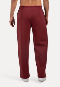 Pantalones de chándal burdeos con cinturilla elástica, bolsillos laterales y un ajuste relajado, mostrando una textura de tela suave.