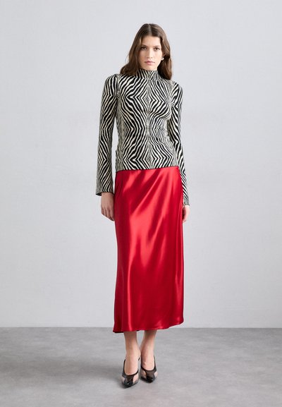 Μαυρόασπρη ριγέ μπλούζα με μακριά μανίκια και ψεύτικο λαιμό, συνδυασμένη με ρέουσα κόκκινη σατέν μάξι φούστα και διάφανα μαύρα τακούνια.