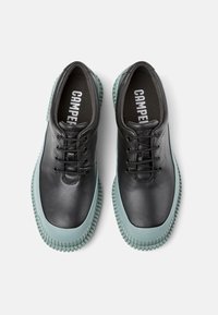 Zapatos de piel negra con punta redondeada, con una suela de goma verde menta, cierre de cordones y logotipo impreso en la plantilla.