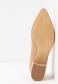 Nude mockafjäll med hög klack, spetsig tå och strukturerad gummisula, med blockklack och präglad logotyp. Storlek 37.