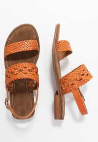 Woven orange leather sandals with two wide straps, a low block heel, and a padded brown insole. Features an adjustable ankle strap.