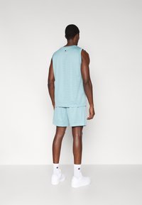 Vaaleansininen urheilutankkitoppi ja shortsit, jotka on valmistettu verkkokankaasta. Takana logo, yhdistetty valkoisiin sukkiin ja lenkkareihin.