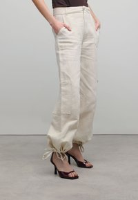 Beige linnen cargobroek met zijzakken, elastische boorden en een ontspannen pasvorm, gecombineerd met glanzende bordeauxrode openhielers.