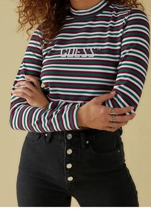 Top à manches longues rayé avec des bandes verticales rouges, vertes et blanches, doté d'un col montant et d'un logo sur la poitrine. Porté avec un jean noir taille haute.