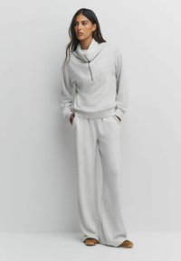 Light gray, cozy sweatshirt with a funnel neck and half zip, paired with wide-leg sweatpants. Soft fabric texture, practical side pockets.