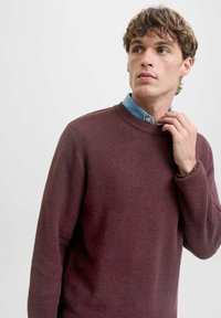 Il maglione a girocollo bordeaux presenta un knit testurizzato, con un colletto in chambray blu chiaro sovrapposto e sottili polsini e orlo a coste.