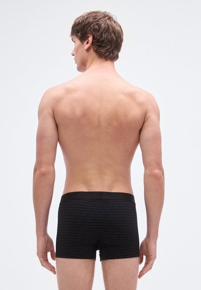 Fekete boxeralsó ismétlődő logómintával, puha anyagból, közepes derékmagassággal és testhezálló fazonnal, hátulnézetben, semleges háttéren.