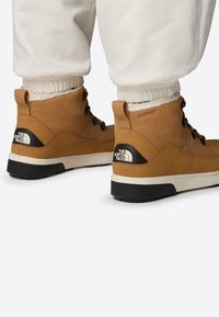 Brown waterproof boots with a textured leather upper, black accents, and a white logo; featuring sturdy laces and a cushioned ankle support.