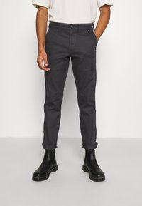 Tmavě šedé bavlněné kalhoty, slim fit s ohrnutými nohavicemi, předními kapsami a mírně viditelnými švy, spárované s černými kotníkovými botami.