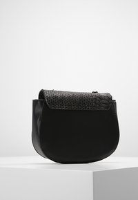 Černá kožená taška se zaobleným tvarem, s texturovaným víkem v černém hadím vzoru a hladkým povrchem. Kompaktní design.