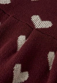 Burgundska pletenina s bijelim uzorcima srca. Mekana tekstura, s ušivenim šavovima i ugodnim izgledom.