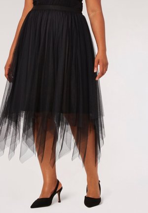 Sort tylskørt med høj-lav søm, elastisk talje, lagdelt tekstur og subtil glans, kombineret med sorte hæle.