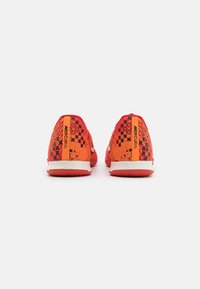 Červené sportovní boty s gradientním designem, obsahující černé vzory, bílé akcenty a výrazné oranžové logo na patě.