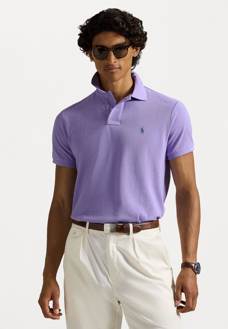 Πολυτελής μοβ πουκάμισο πόλο με υφή και κολάρο δύο κουμπιών, σε συνδυασμό με κρέμα παντελόνι και καφέ ζώνη. Φανερή λεπτομέρεια λογότυπου στο στήθος.