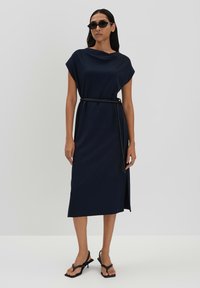 Marineblaue, knielange Kleid mit kurzen Ärmeln, taillierter Taille und einem seitlichen Schlitz. Getragen mit schwarzen, schmalen Riemensandalen mit Absatz und Sonnenbrille.