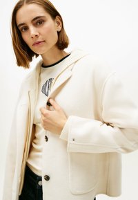 Roomkleurig jack met een gestructureerde afwerking, voorzien van een capuchon, geribbelde manchetten en grote knopen. Casual ontwerp met zakken met klep.