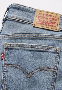 Poche arrière d'un jean en denim bleu clair avec l'onglet rouge Levi's et un patch en cuir beige Levi Strauss & Co. montrant deux chevaux tirant sur un jean.