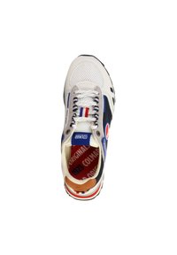 Zapatilla deportiva blanca con parte superior de malla, acentos en azul marino y una pestaña en el talón de color marrón. Plantilla roja con texto; logo azul cerca de la lengüeta. Suela de goma.