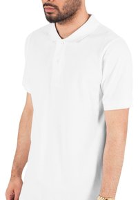 Cămașă polo albă cu guler clasic, mâneci scurte și placket cu trei butoane. Material moale, design minimal și fără modele.