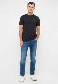 Czarny bawełniany T-shirt z okrągłym dekoltem, z małym białym logo, w połączeniu z jasnoniebieskimi dżinsami i białymi trampkami.