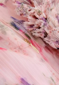 Kerge roosa tüllkangas, millel on lilleseaded lilla ja rohelise värviga. Omab volangilisi ääri ja väikest kuldset lukku.