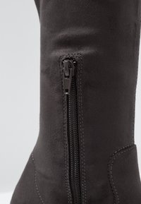 Bota alta de ante negra con cremallera lateral, costuras en contraste y un diseño elegante con puntera redonda.