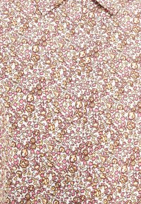 Camicetta floreale con base bianca, decorata con fiori rosa e marroni e dettagli verdi; motivo floreale piccolo e dettagliato su tutta la superficie.