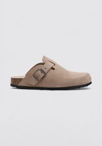 Sabots en cuir suédé beige avec un bout arrondi, une boucle réglable et une semelle semblable au liège. Surface texturée et semelle extérieure en caoutchouc noir pour l'adhérence.