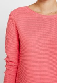 Różowy sweter z prążkowanej dzianiny z okrągłym dekoltem i długimi rękawami z subtelnym zagięciem przy mankietach, wykonany z teksturowanej dzianiny.