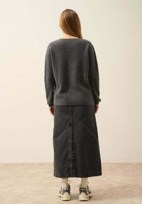 Szary sweter dzianinowy o luźnym kroju, zestawiony z długą spódnicą z ciemnego dżinsu z rozporgiem z tyłu. Noszony z kremowo-czarnymi sneakery.