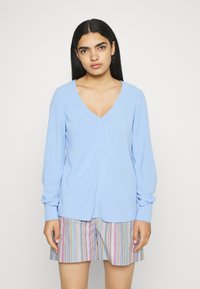 Sweater de manga longa azul clara com decote em V e mangas franzidas, combinado com calções às riscas em várias cores pastéis.