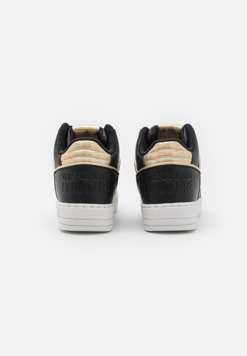 Sneakers low-top in pelle nera con suola in gomma bianca, caratterizzati da un pannello superiore iridescente dorato e logo in rilievo sul tallone.