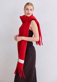 Rode wollen sjaal met franjes aan de uiteinden en een vlak gebreid ontwerp. Voorzien van een wit label met "ARCTIC FOX" merknaam.
