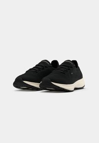 Black athletic shoes with a textured mesh upper, flat laces, and a contrasting cream sole. Features a minimalistic design with a flexible outsole.
