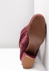 Botte chelsea en daim bordeaux avec un bout arrondi, une fermeture éclair latérale et une semelle en caoutchouc texturé. Présente un talon bloc de hauteur moyenne.